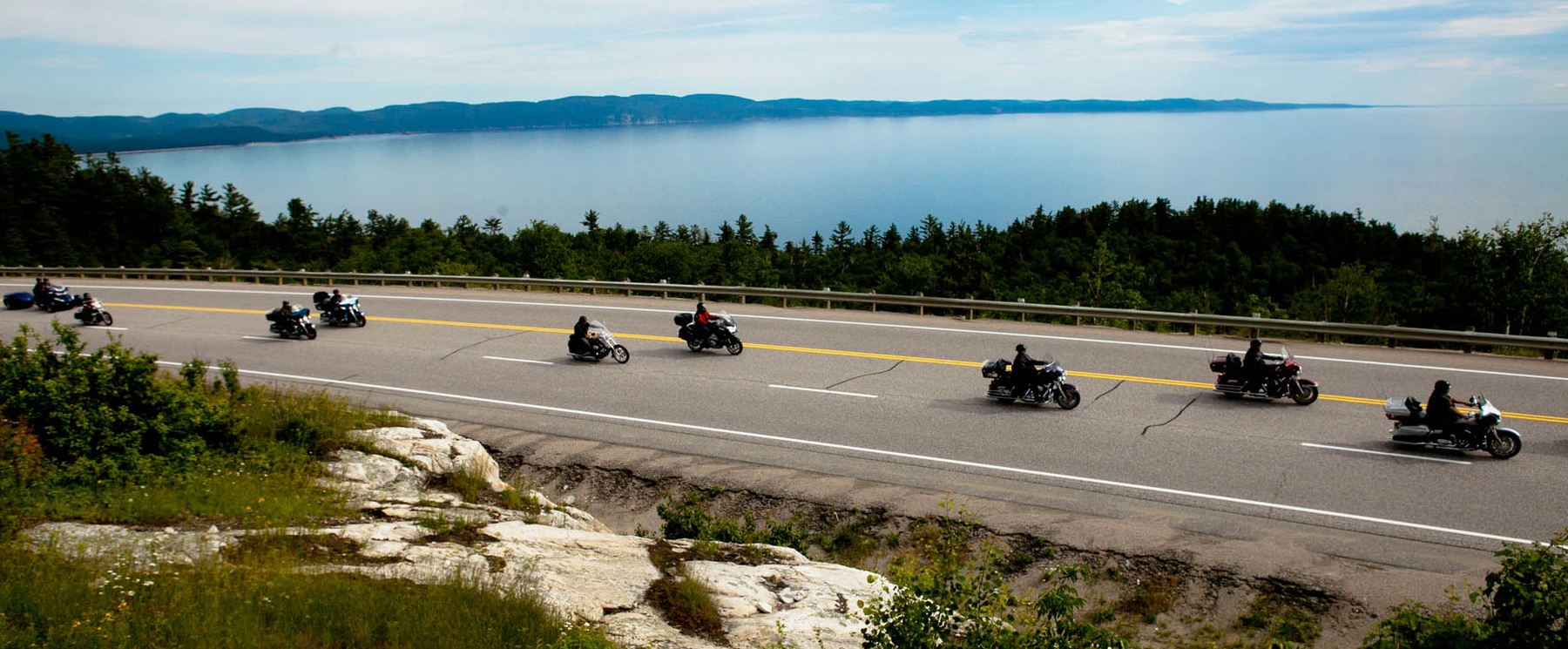 A group of motorcycle riders cruise along the shore of Lake Superior