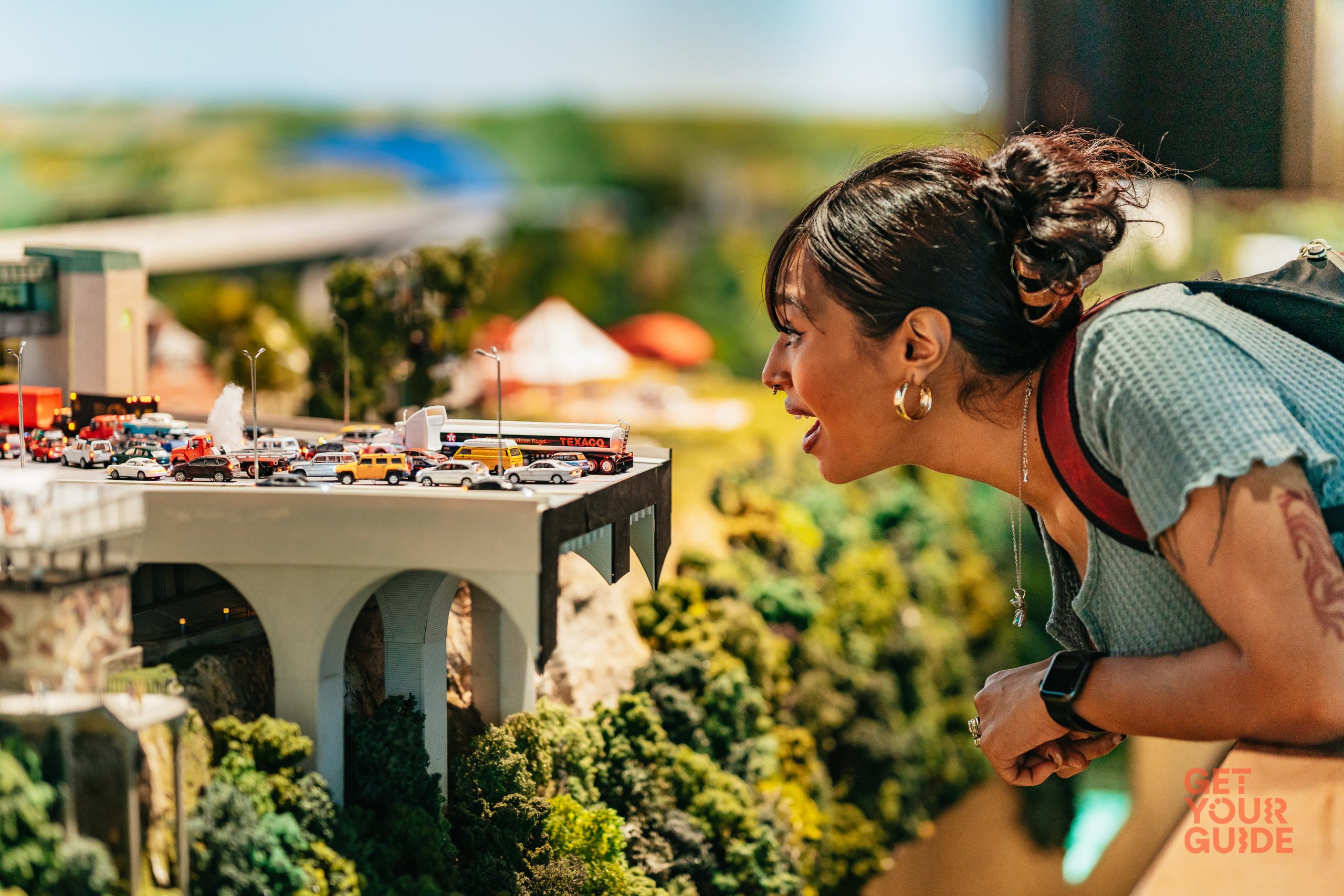 A women is leaning forward looking closely at a small bridge filled with tiny little cars