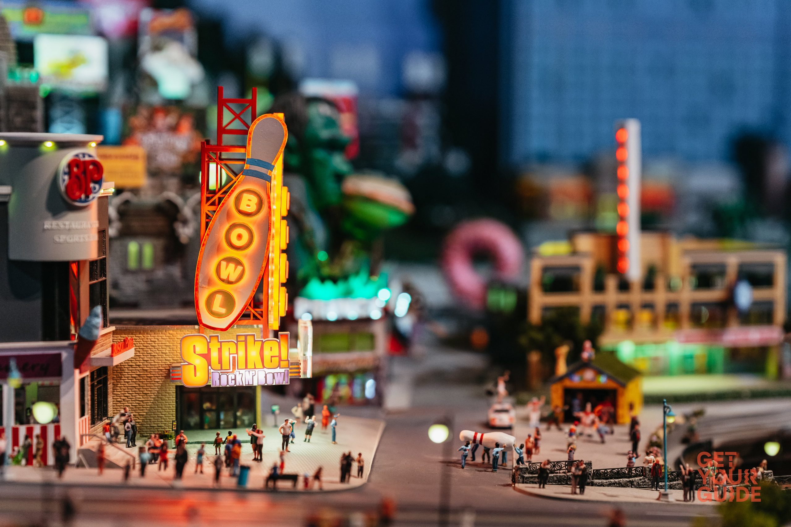 A miniature scene showing a bowling alley entrance, along with a tiny group of people carrying a large bowling pin.